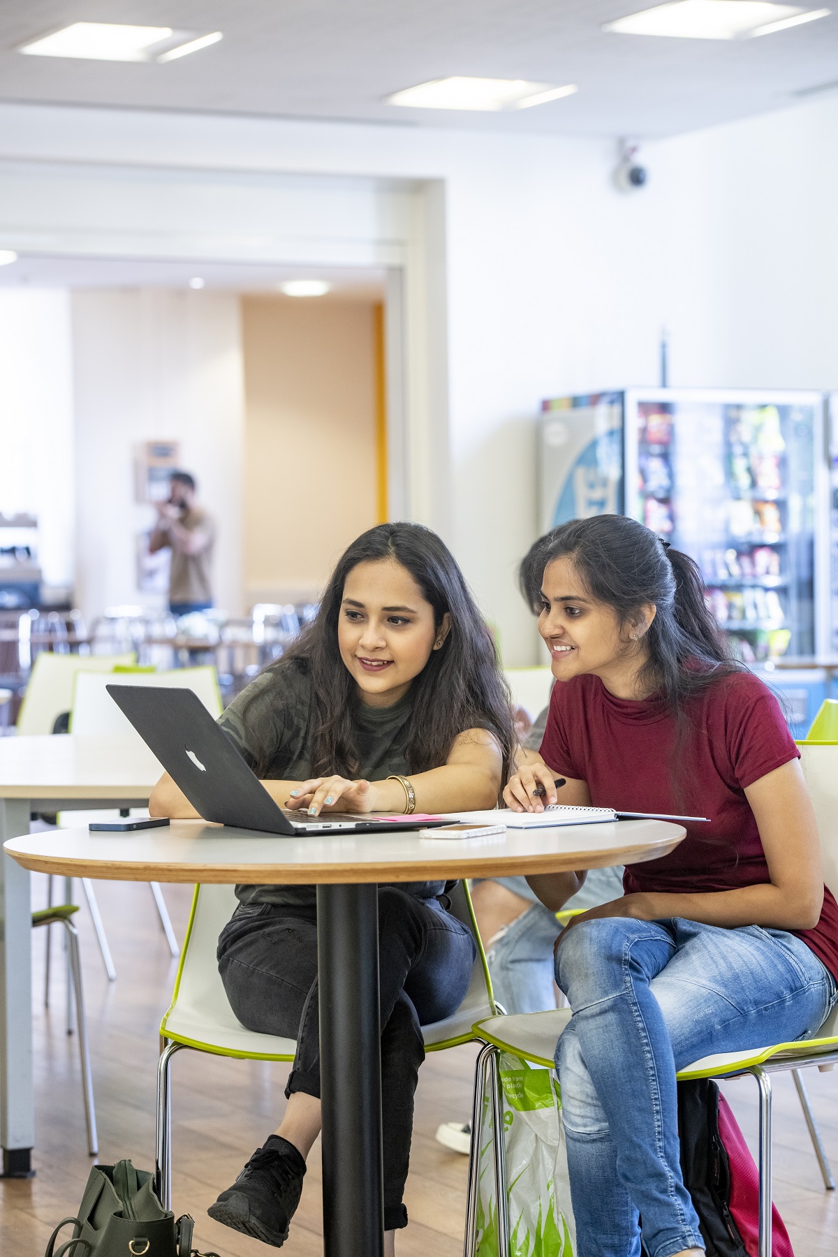 Two female students working around a small table on a single laptop