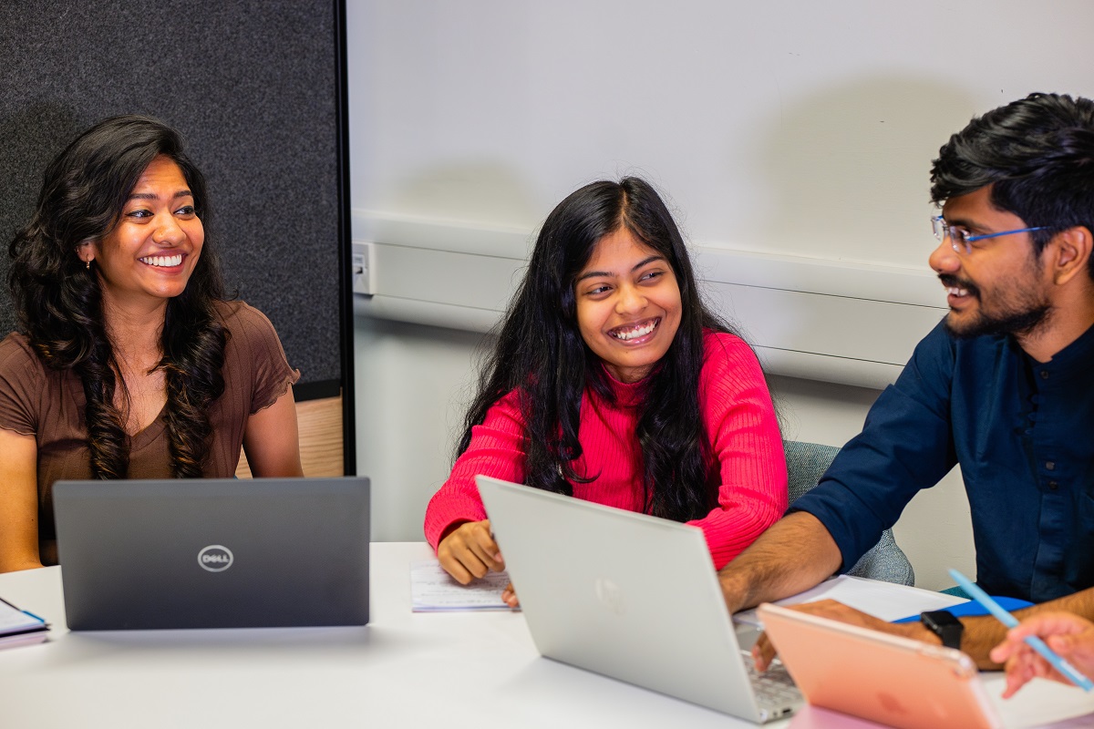 Group of students in discussion around a table with laptops and tablets